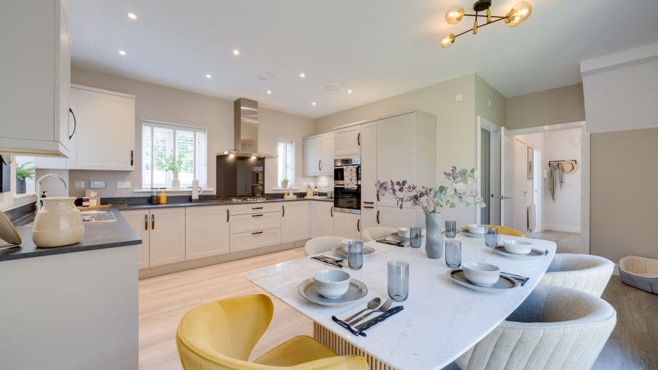 Interior view of open-plan kitchen with cream units, dark worktops and wood effect flooring.