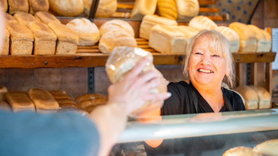 A smiling lady in the high street bakery serving a customer.