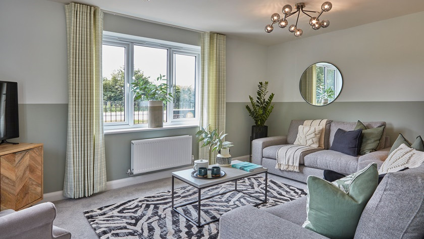 A neutral themes lounge with grey sofas and sage green curtains, cushions and wall paint, with a black and white zebra print rug and a coffee table