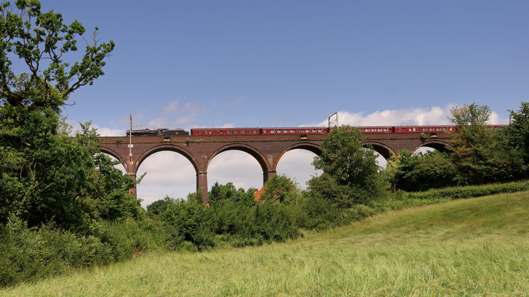 Tall railway bridge with archways in a grassy landscape with a red train passing by