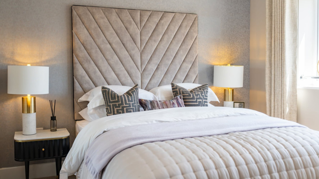 Bedroom with double bed, soft cushioned headboard and bedside tables with lamps on