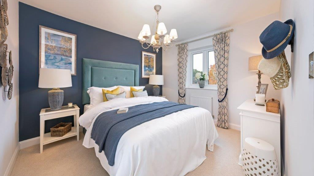 A bedroom with a double bed, a grey-blue feature wall, and bedroom furniture