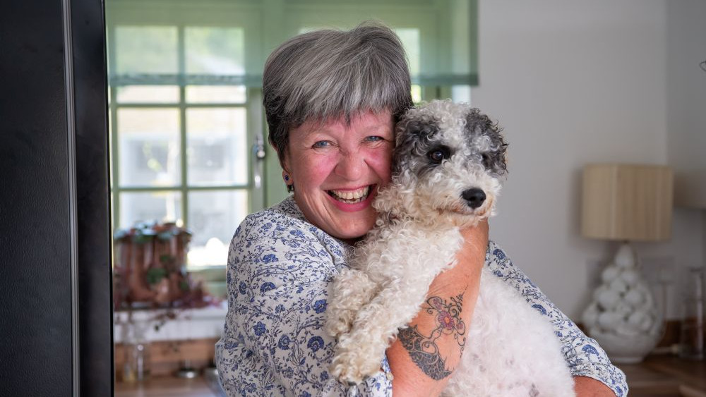 A lady smiling and holding her beloved dog in her lounge